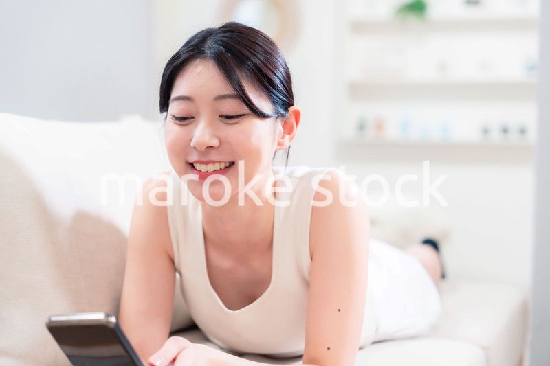 ソファで寝転がってスマホを使う若い女性