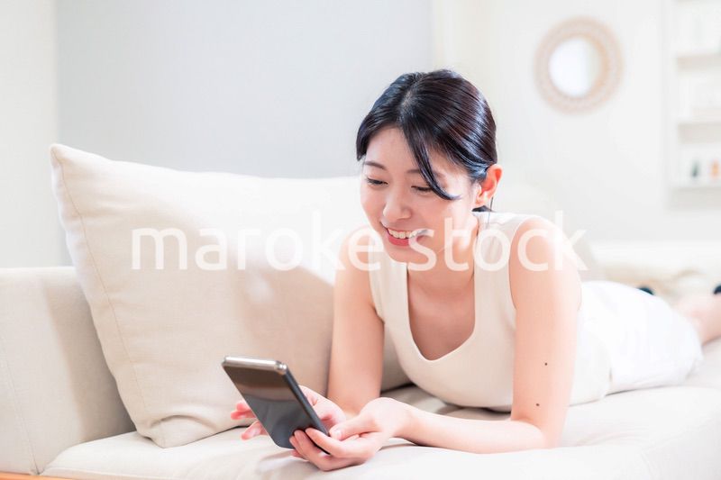 ソファで寝転がってスマホを使う若い女性
