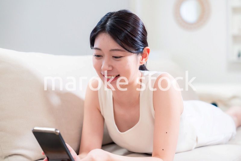 ソファで寝転がってスマホを使う若い女性