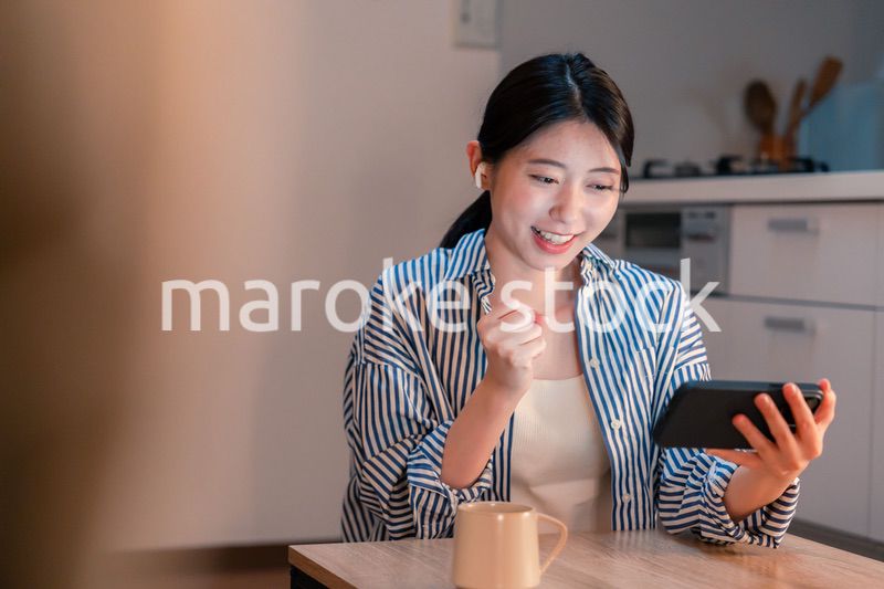 夜に家でスマホでスポーツ観戦をする若い女性