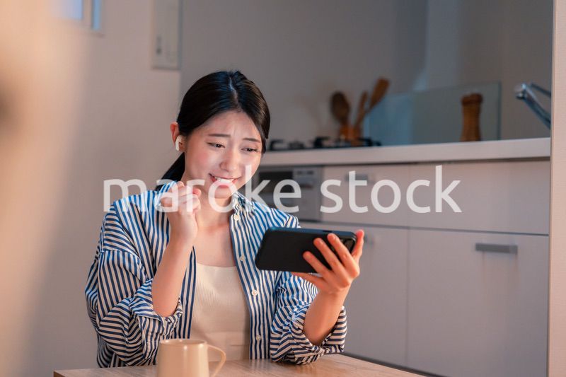 夜に家でスマホでスポーツ観戦をする若い女性