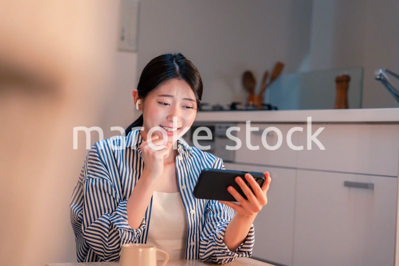 夜に家でスマホでスポーツ観戦をする若い女性