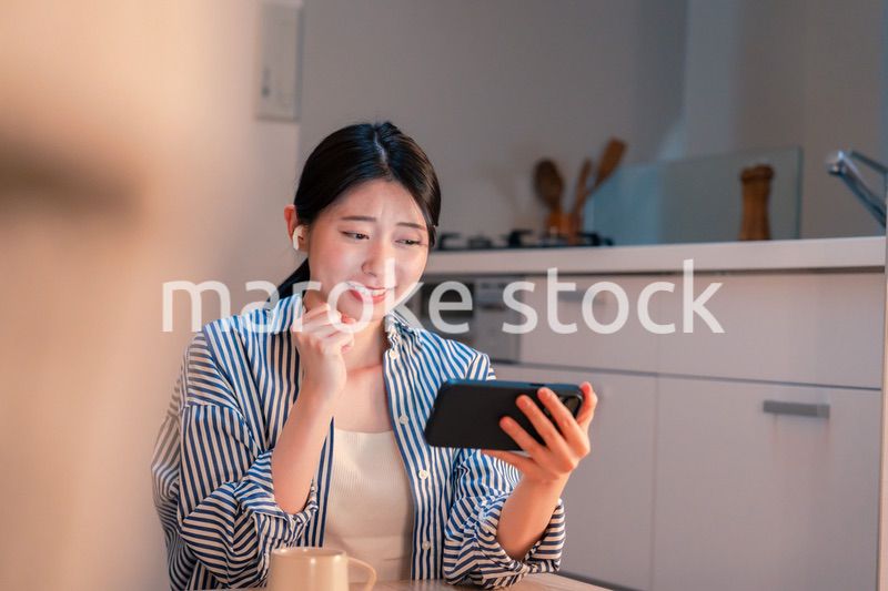 夜に家でスマホでスポーツ観戦をする若い女性