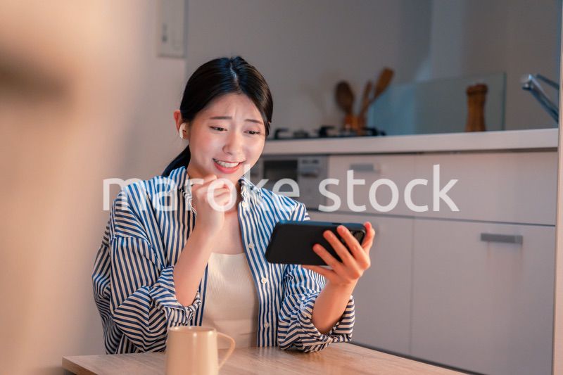 夜に家でスマホでスポーツ観戦をする若い女性