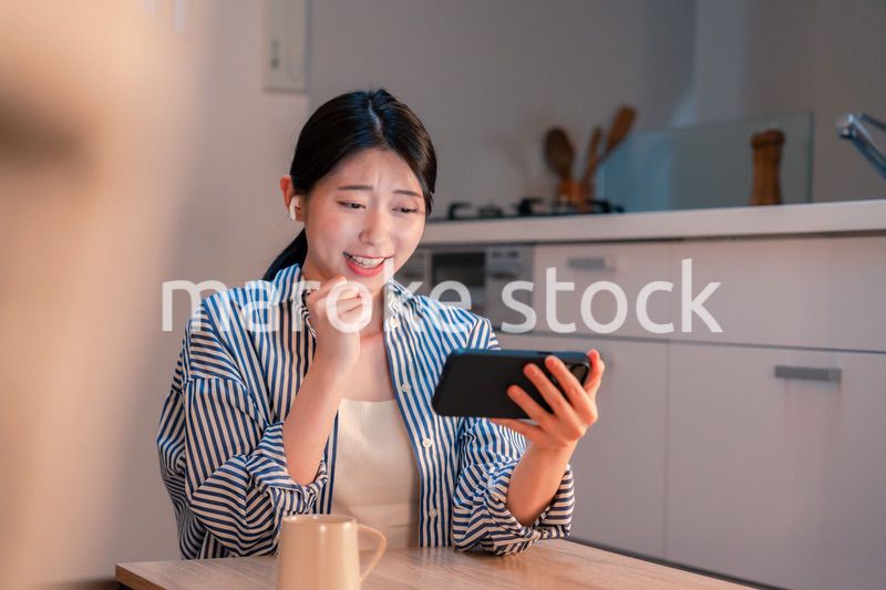 夜に家でスマホでスポーツ観戦をする若い女性