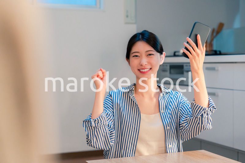 家で夜にスマホを持って大喜びをする若い女性