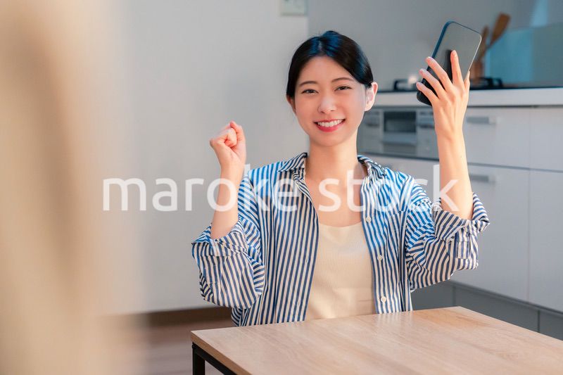 家で夜にスマホを持って大喜びをする若い女性