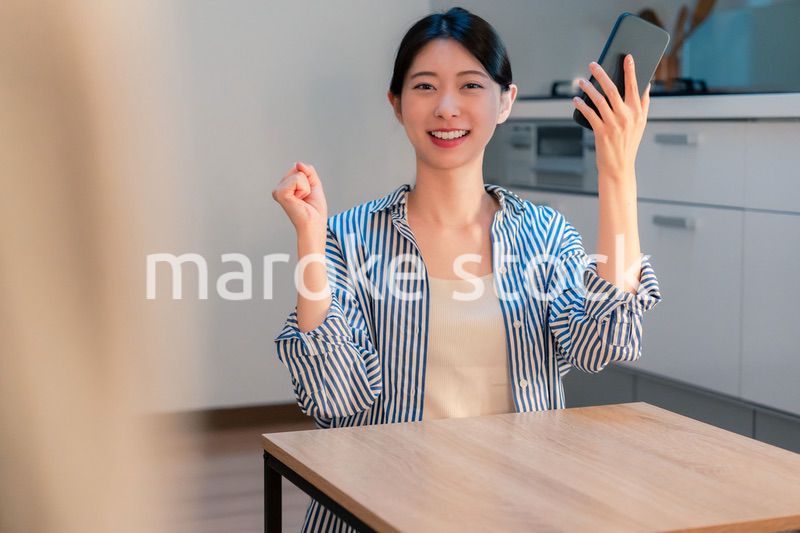 家で夜にスマホを持って大喜びをする若い女性