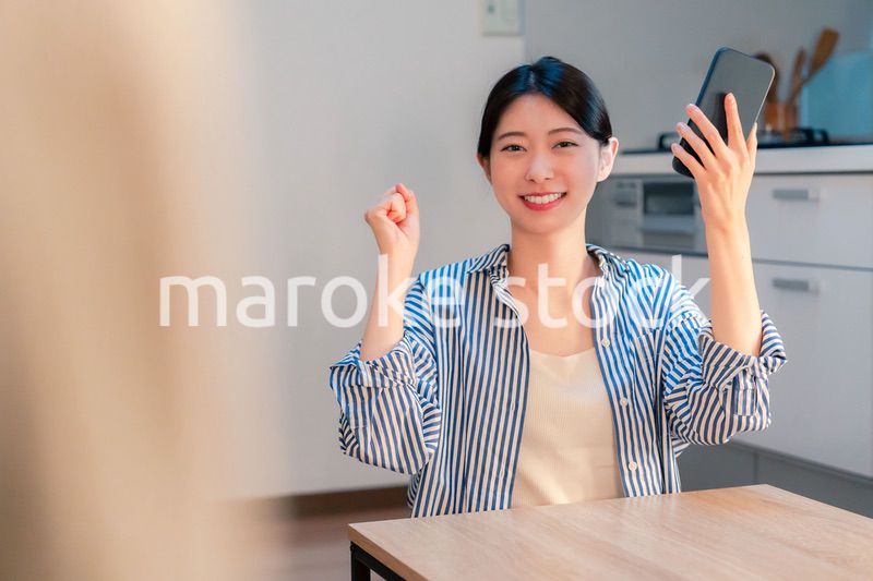 家で夜にスマホを持って大喜びをする若い女性
