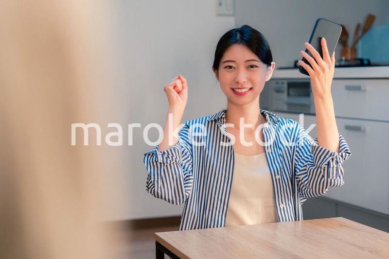 家で夜にスマホを持って大喜びをする若い女性