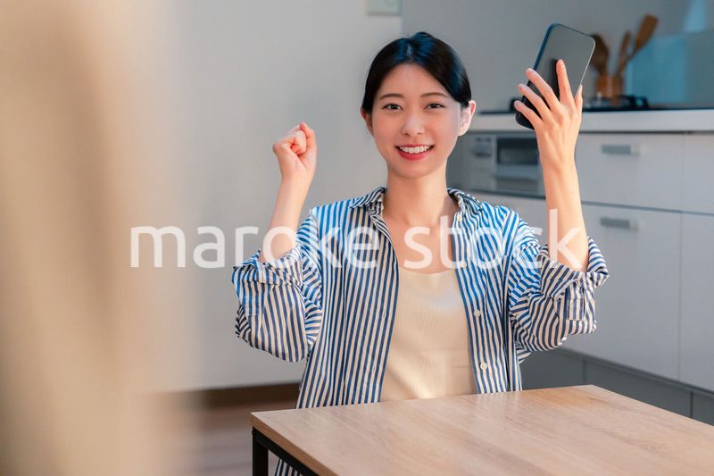 家で夜にスマホを持って大喜びをする若い女性