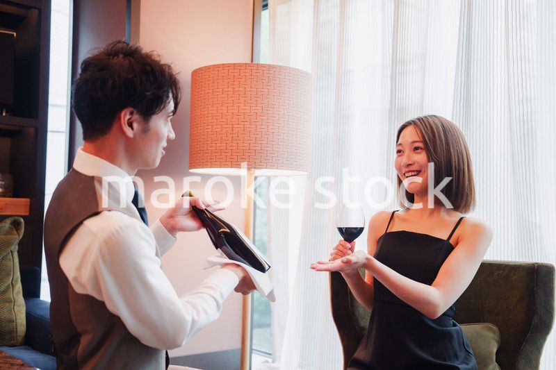ホテルのルームサービスで女性にワインを提供する男性スタッフ
