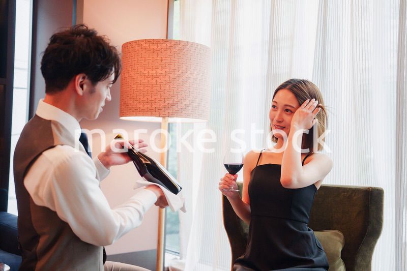 ホテルのルームサービスで女性にワインを提供する男性スタッフ