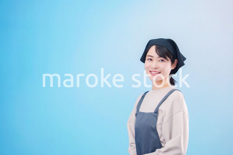 エプロンを着た調理師の若い女性（水色背景）