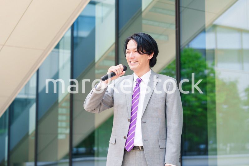 マイクを使って街なかで演説をするスーツを着た男性