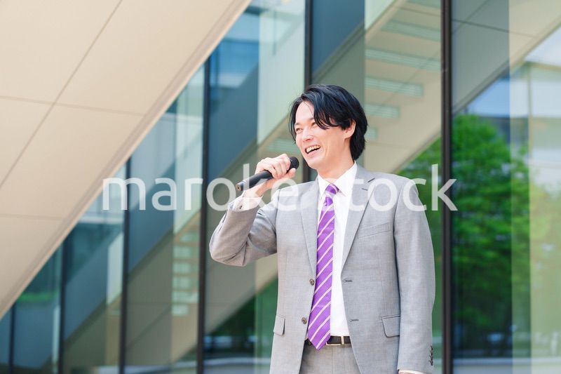 マイクを使って街なかで演説をするスーツを着た男性