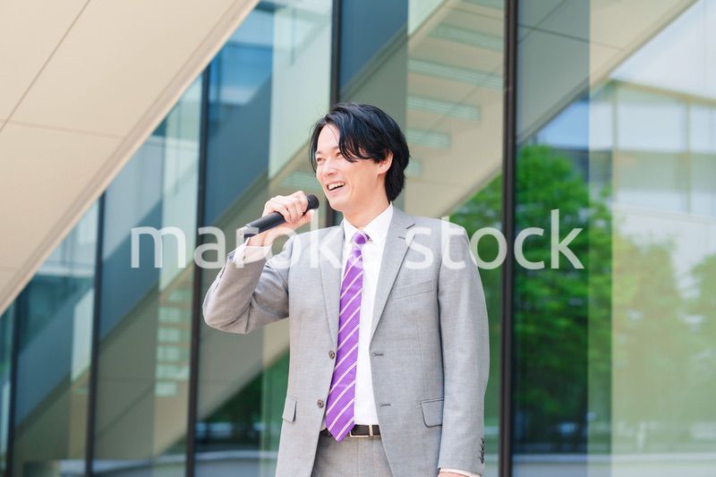 マイクを使って街なかで演説をするスーツを着た男性