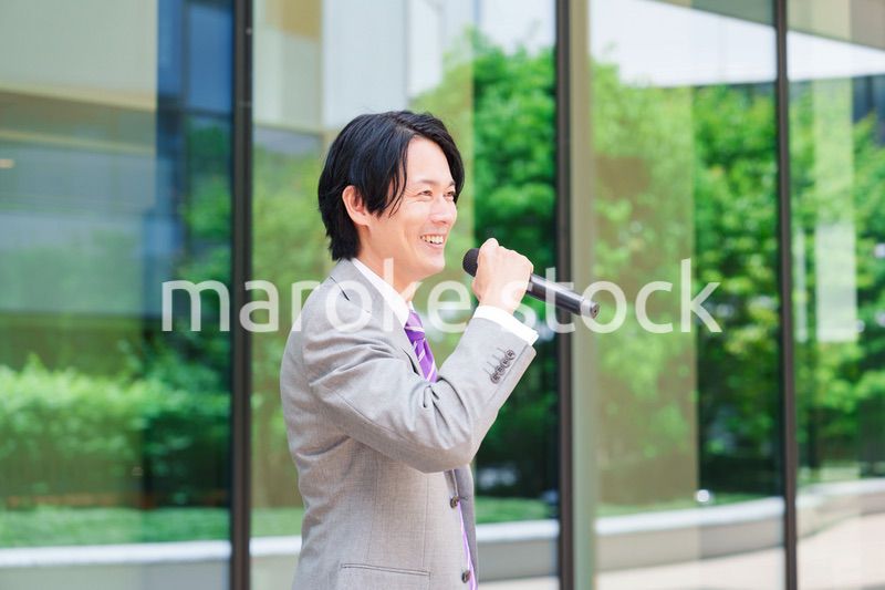 マイクを使って街なかで演説をするスーツを着た男性