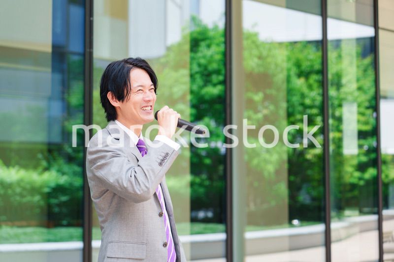 マイクを使って街なかで演説をするスーツを着た男性