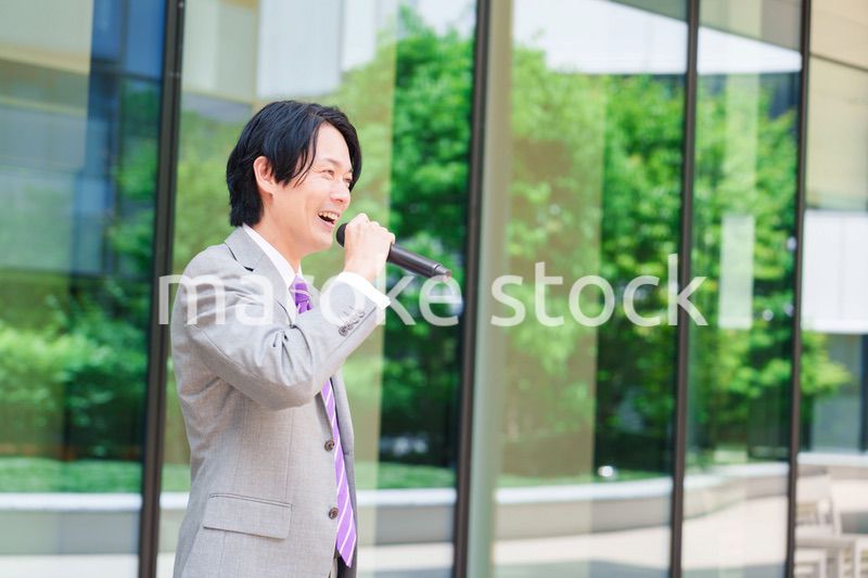 マイクを使って街なかで演説をするスーツを着た男性