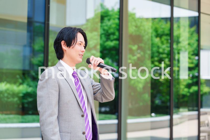 マイクを使って街なかで演説をするスーツを着た男性