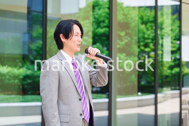 マイクを使って街なかで演説をするスーツを着た男性