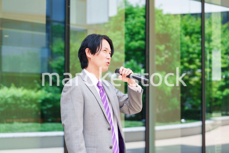 マイクを使って街なかで演説をするスーツを着た男性