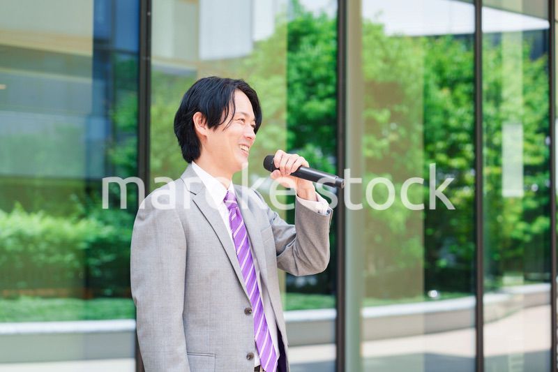 マイクを使って街なかで演説をするスーツを着た男性