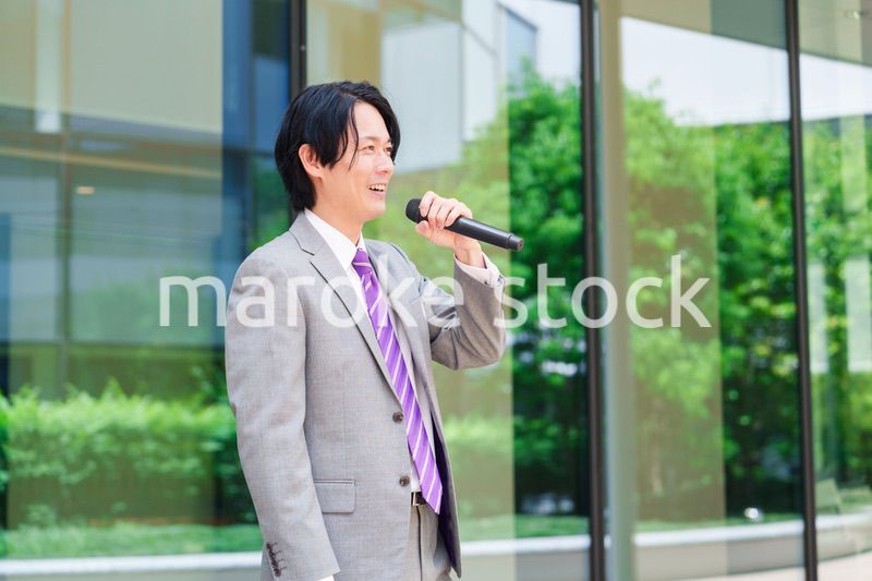 マイクを使って街なかで演説をするスーツを着た男性