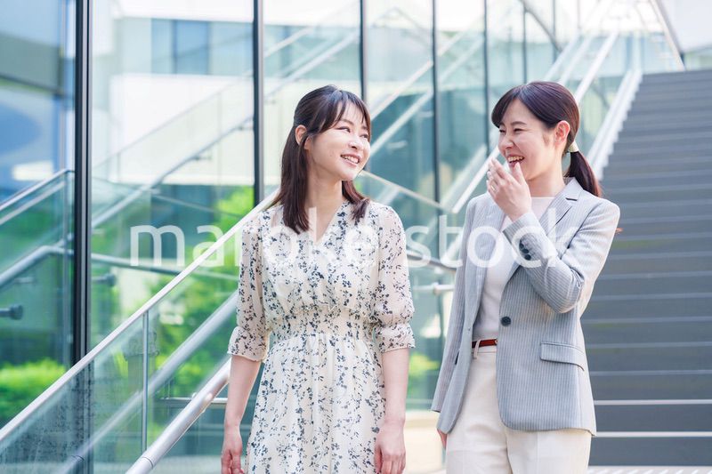 楽しく話しながらオフィスの中を歩く女性ビジネスパーソン