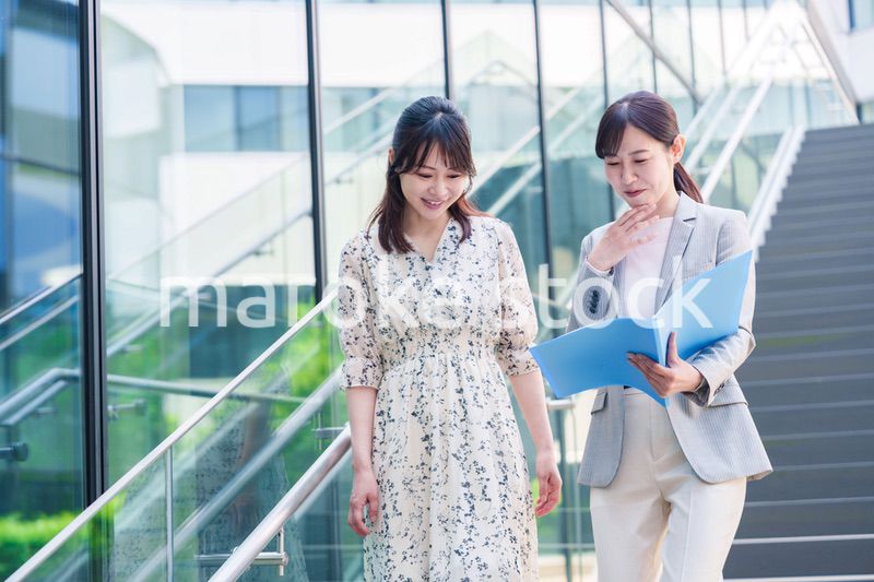 楽しく話しながらオフィスの中を歩く女性ビジネスパーソン