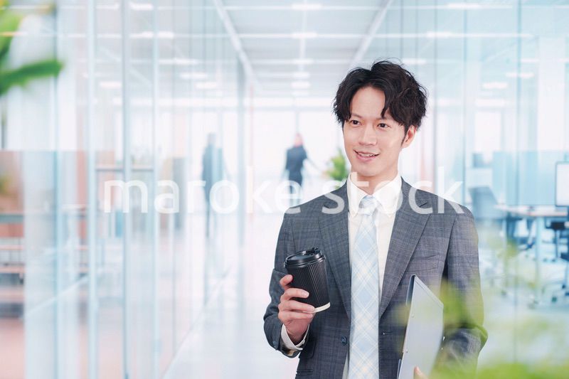 オフィスで紙カップのコーヒーを持って歩くビジネスマン