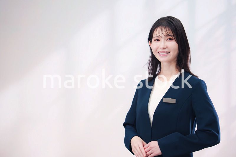 名札をつけて笑顔で接客をする若い女性（シンプル背景）