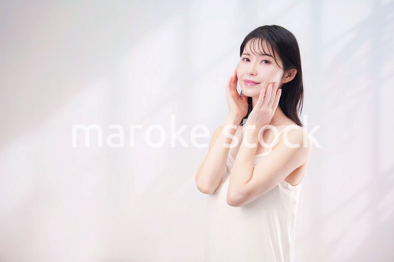 笑顔でお肌のケアをする若い女性（シンプル背景）