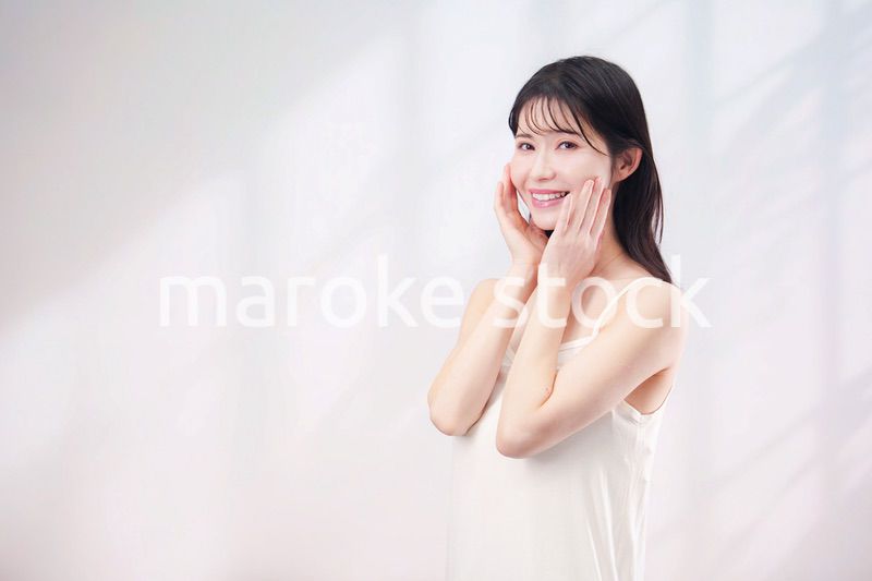 笑顔でお肌のケアをする若い女性（シンプル背景）