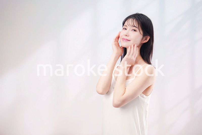 笑顔でお肌のケアをする若い女性（シンプル背景）