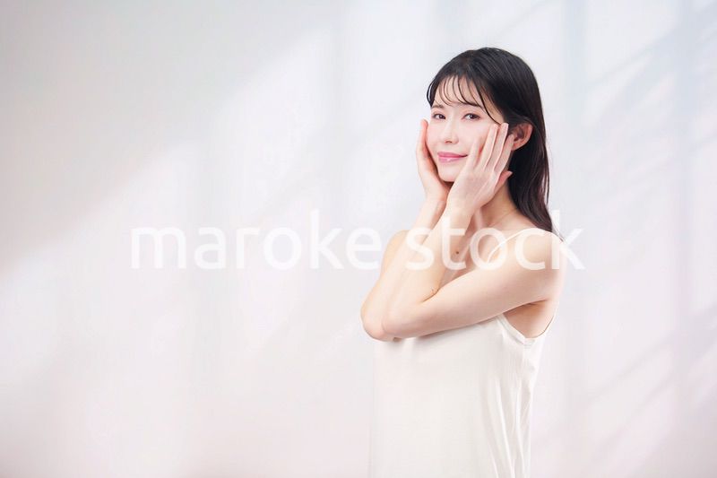 笑顔でお肌のケアをする若い女性（シンプル背景）