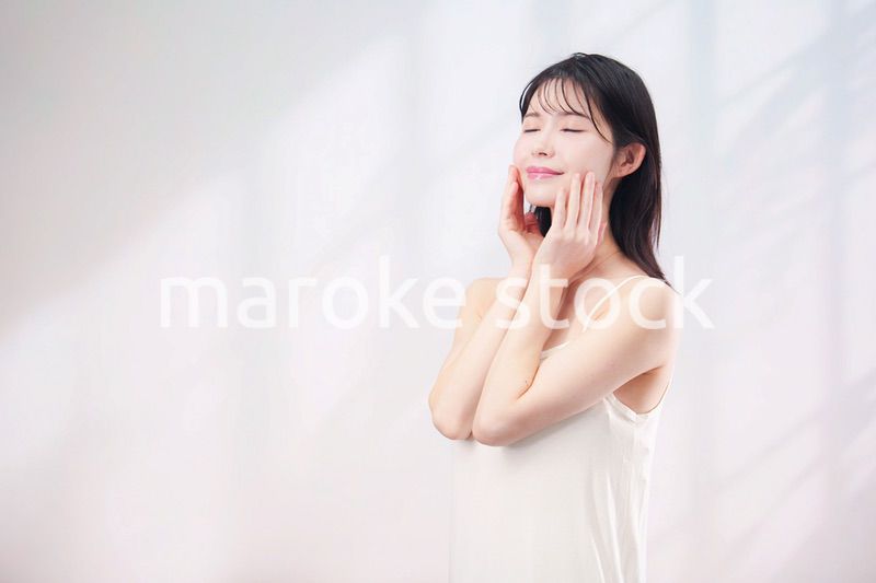 笑顔でお肌のケアをする若い女性（シンプル背景）