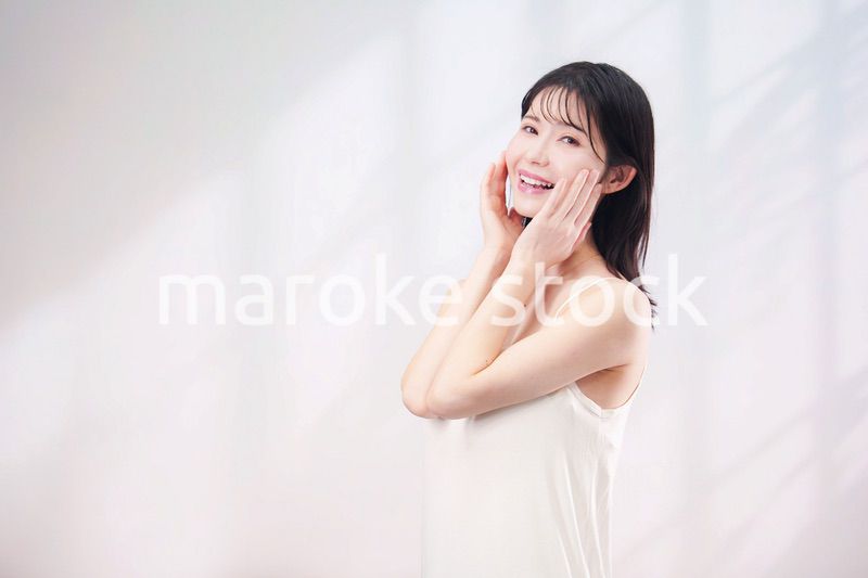 笑顔でお肌のケアをする若い女性（シンプル背景）