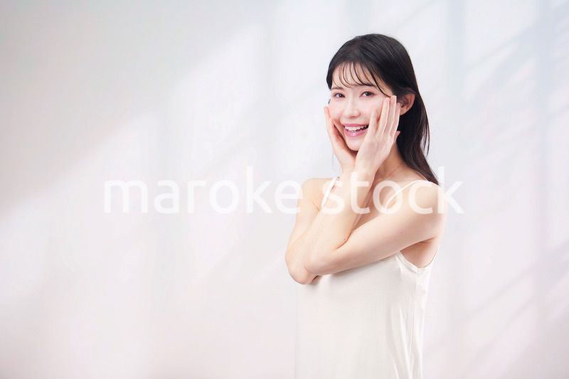 笑顔でお肌のケアをする若い女性（シンプル背景）