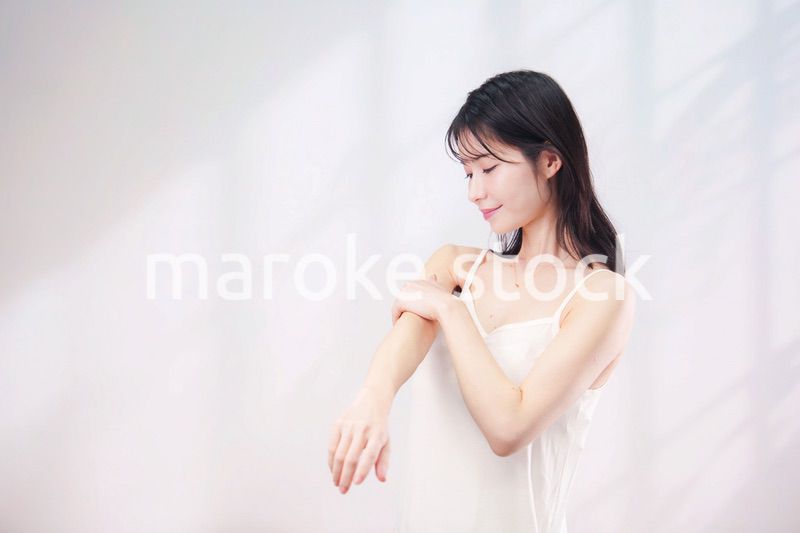 腕にクリームを塗る若い女性（シンプル背景）
