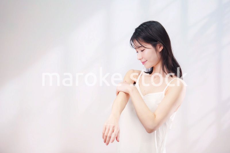 腕にクリームを塗る若い女性（シンプル背景）