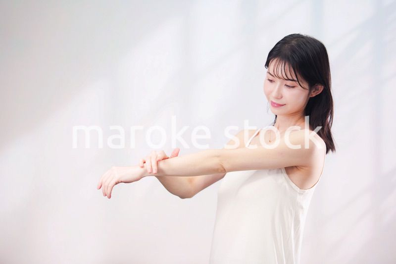 腕にクリームを塗る若い女性（シンプル背景）