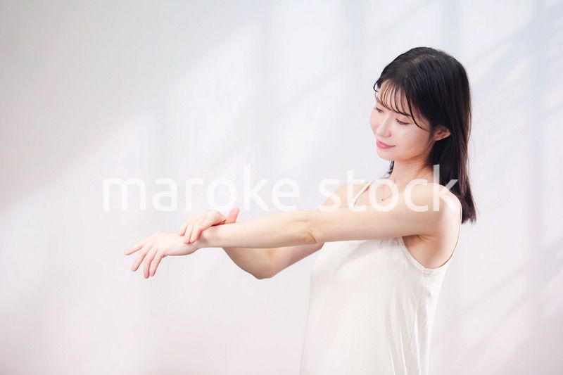 腕にクリームを塗る若い女性（シンプル背景）