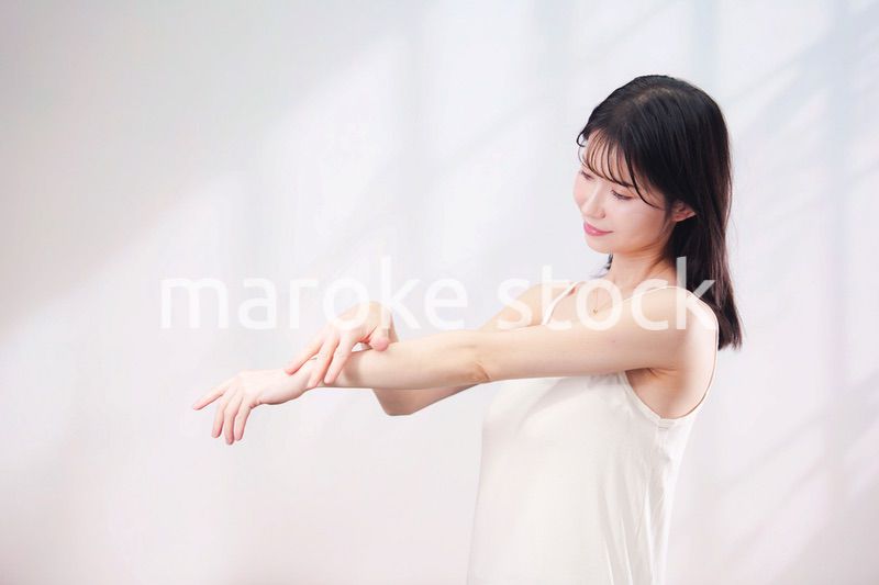 腕にクリームを塗る若い女性（シンプル背景）