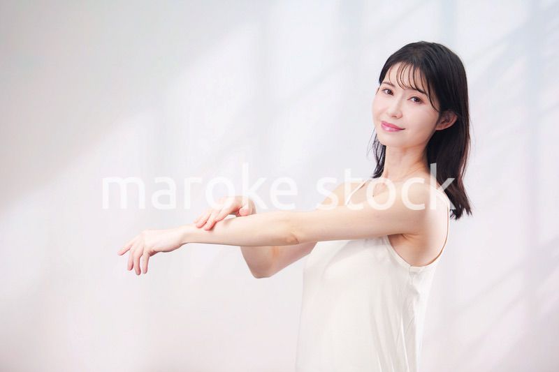 腕にクリームを塗る若い女性（シンプル背景）