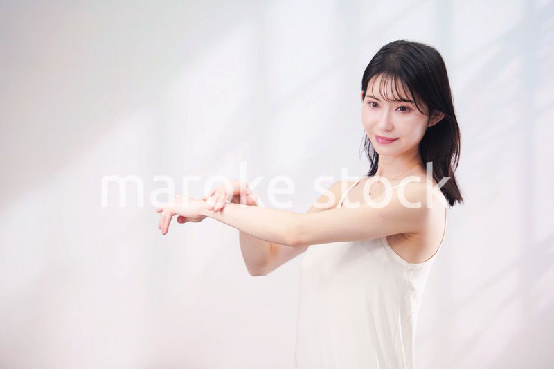 腕にクリームを塗る若い女性（シンプル背景）