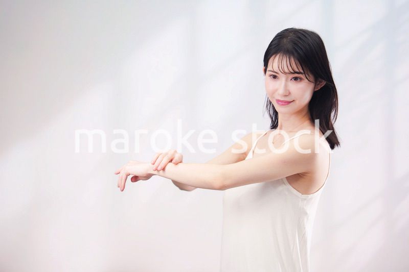 腕にクリームを塗る若い女性（シンプル背景）