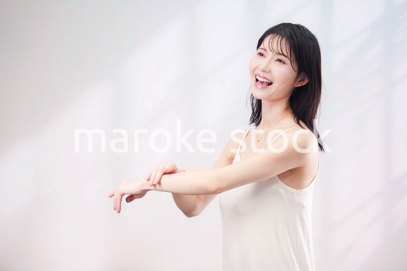 腕にクリームを塗る若い女性（シンプル背景）