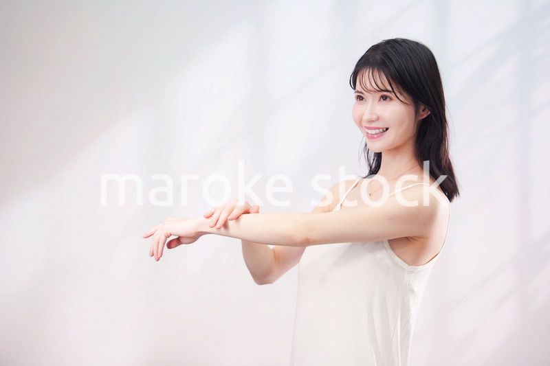 腕にクリームを塗る若い女性（シンプル背景）